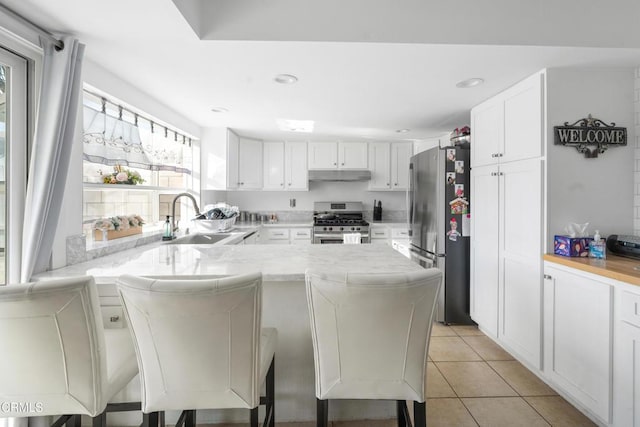 kitchen featuring kitchen peninsula, white cabinetry, a kitchen breakfast bar, stainless steel appliances, and light tile patterned floors