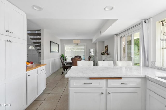 kitchen featuring light tile patterned floors, light stone countertops, white cabinets, and kitchen peninsula