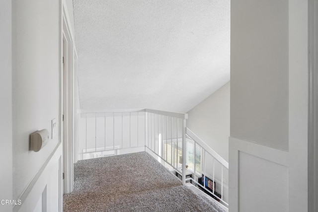 stairway with lofted ceiling, a textured ceiling, and carpet flooring