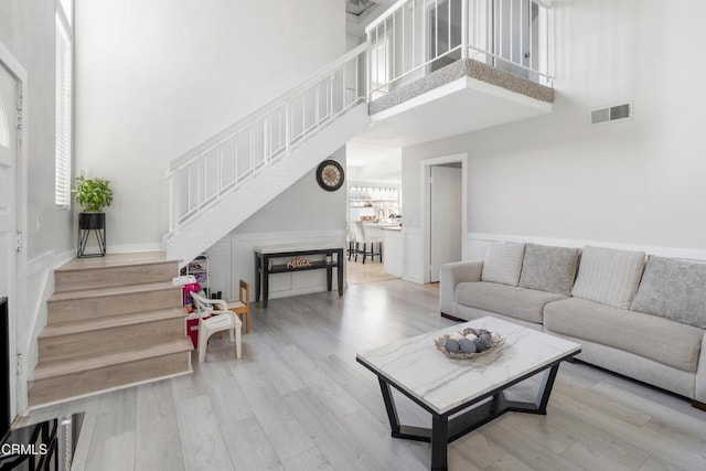 living area with wood finished floors, visible vents, a towering ceiling, and stairs