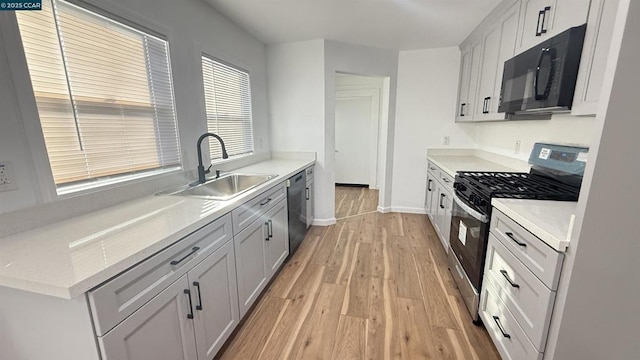 kitchen featuring light stone countertops, sink, light hardwood / wood-style floors, and black appliances