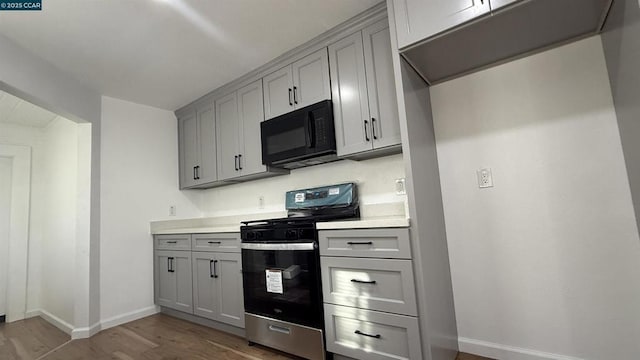 kitchen featuring stainless steel gas stove, wood-type flooring, and gray cabinets