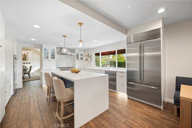 kitchen with white cabinetry, stainless steel built in fridge, wall chimney range hood, pendant lighting, and a center island