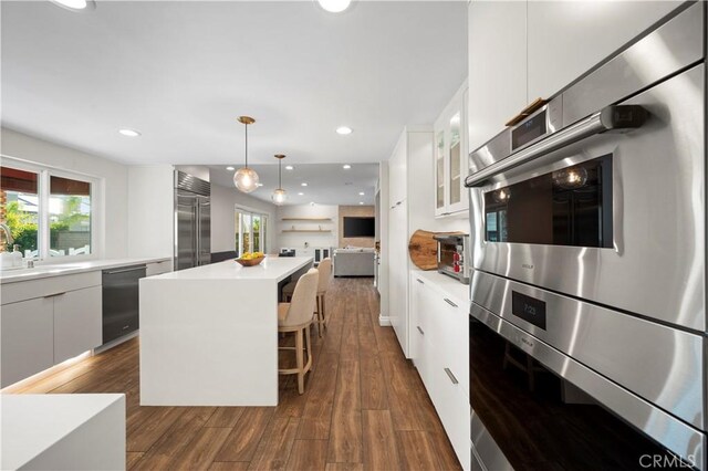 kitchen with white cabinetry, appliances with stainless steel finishes, decorative light fixtures, a kitchen island, and a breakfast bar