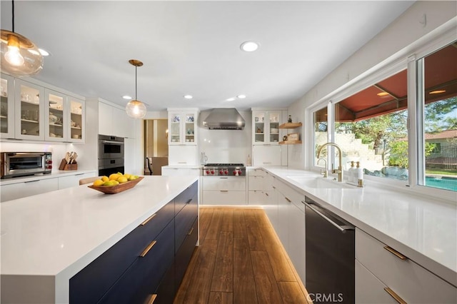 kitchen featuring white cabinetry, appliances with stainless steel finishes, wall chimney range hood, pendant lighting, and sink