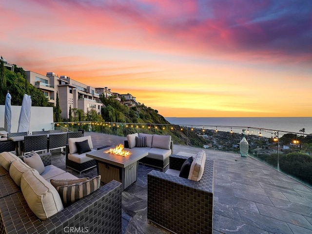 patio terrace at dusk featuring a water view and an outdoor living space with a fire pit