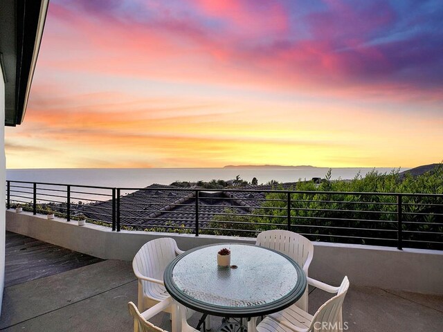 balcony at dusk featuring a water view