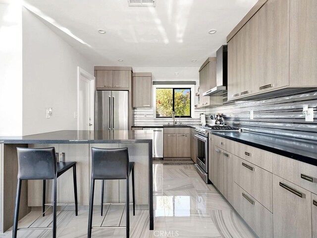 kitchen featuring light brown cabinets, a kitchen bar, wall chimney range hood, and high quality appliances