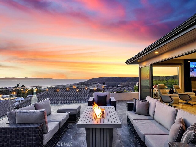 patio terrace at dusk with a water and mountain view and an outdoor living space with a fire pit