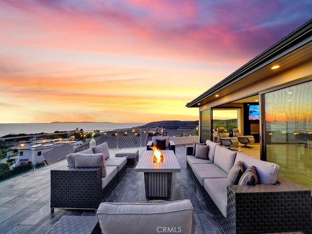 patio terrace at dusk with a water view and an outdoor living space with a fire pit