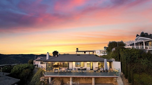 back house at dusk featuring a mountain view and a patio