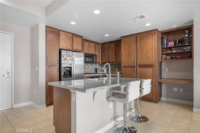 kitchen with appliances with stainless steel finishes, dark stone countertops, an island with sink, sink, and a breakfast bar