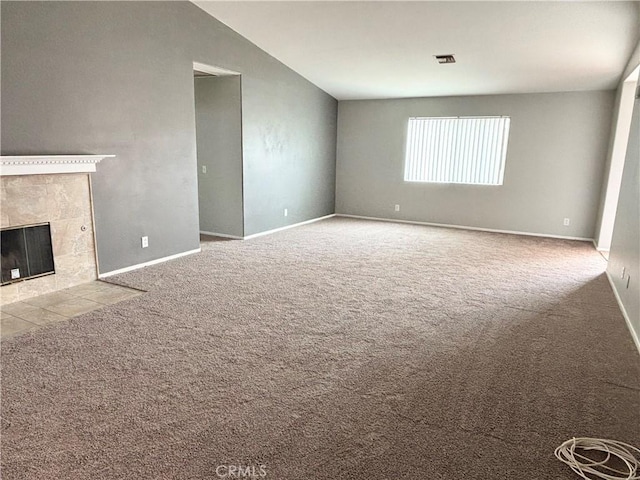 unfurnished living room with a tiled fireplace, vaulted ceiling, and light carpet