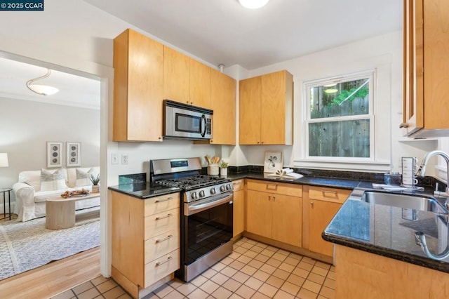 kitchen with sink, dark stone counters, light tile patterned floors, stainless steel appliances, and light brown cabinets