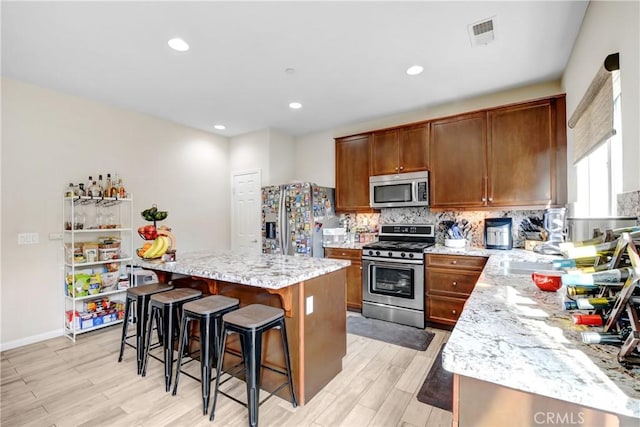 kitchen featuring light stone countertops, a kitchen island, stainless steel appliances, a kitchen breakfast bar, and light wood-type flooring