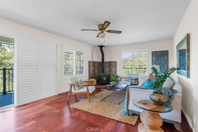 living room featuring hardwood / wood-style flooring, ceiling fan, a wealth of natural light, and a wood stove