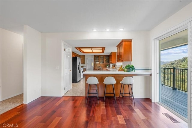 kitchen featuring dark hardwood / wood-style floors, a breakfast bar, kitchen peninsula, and stainless steel refrigerator with ice dispenser