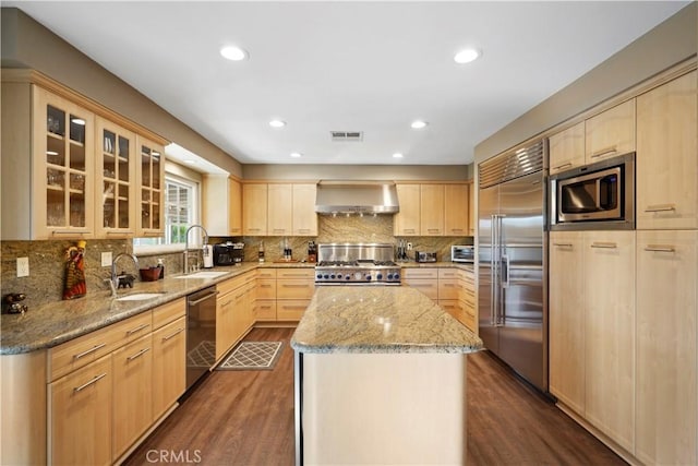 kitchen with sink, wall chimney range hood, built in appliances, and a kitchen island