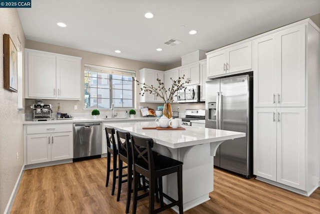 kitchen with white cabinetry, a kitchen bar, appliances with stainless steel finishes, light hardwood / wood-style flooring, and sink