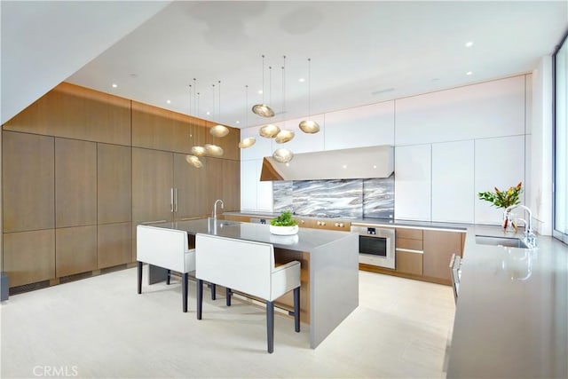 kitchen with sink, white cabinets, a kitchen bar, stainless steel oven, and a spacious island