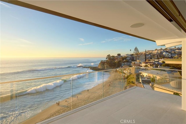 balcony at dusk featuring a water view and a beach view