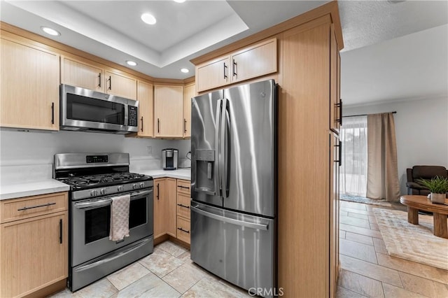 kitchen with light brown cabinets, a raised ceiling, and appliances with stainless steel finishes