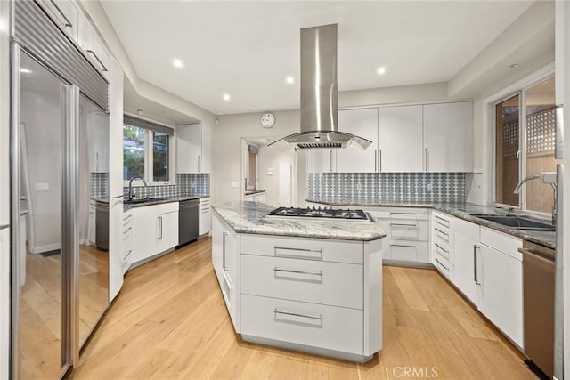 kitchen with a center island, white cabinetry, appliances with stainless steel finishes, island range hood, and light stone counters