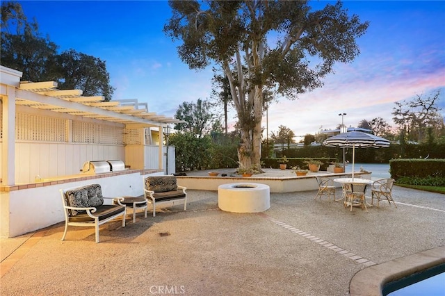 patio terrace at dusk featuring a pergola and exterior kitchen