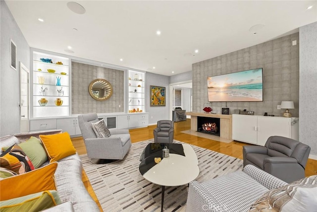 living room featuring light hardwood / wood-style flooring, built in features, tile walls, and a fireplace