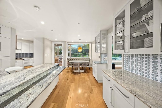 kitchen with decorative light fixtures, decorative backsplash, light hardwood / wood-style flooring, white cabinets, and light stone counters