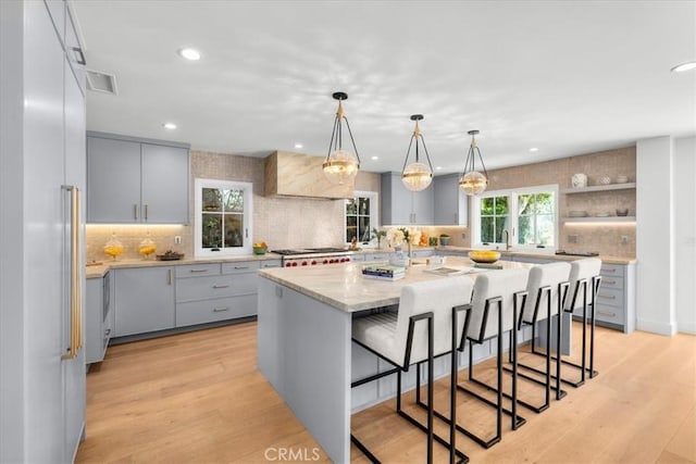 kitchen featuring pendant lighting, a kitchen breakfast bar, a center island with sink, and gray cabinetry