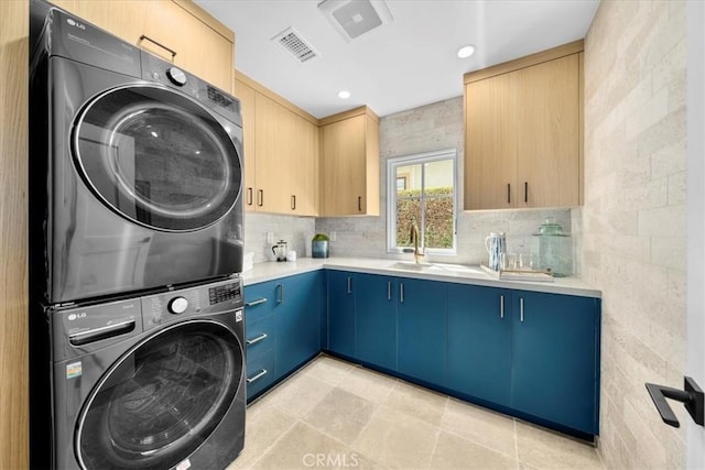 clothes washing area featuring stacked washer and dryer, sink, light tile patterned floors, and cabinets