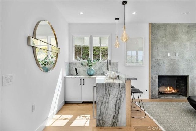 bar with a tile fireplace, light hardwood / wood-style flooring, white cabinets, and decorative light fixtures