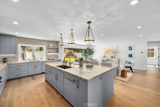 kitchen featuring hanging light fixtures, sink, a center island with sink, and gray cabinetry