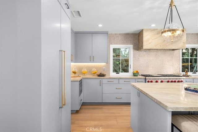 kitchen featuring gray cabinets, a breakfast bar, decorative backsplash, hanging light fixtures, and light hardwood / wood-style flooring