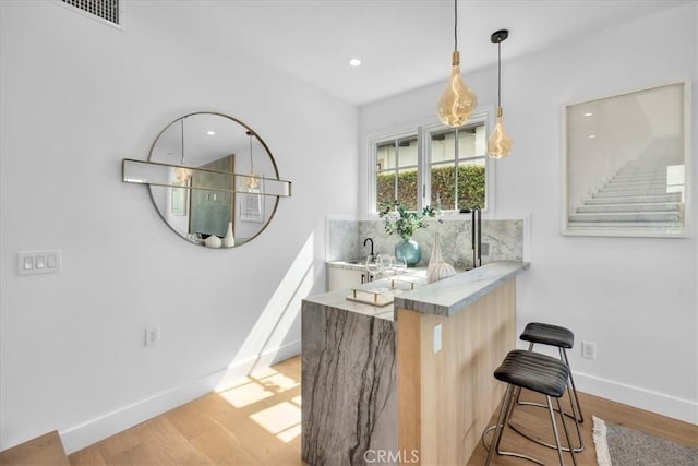 bar with backsplash, light hardwood / wood-style flooring, and hanging light fixtures