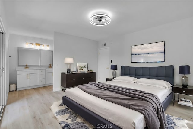 bedroom with light wood-type flooring, sink, and ensuite bath