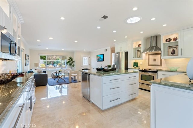 kitchen with stainless steel appliances, white cabinets, a kitchen island, and wall chimney range hood