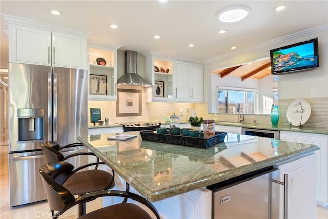 kitchen featuring stainless steel appliances, white cabinetry, a kitchen island, and wall chimney range hood