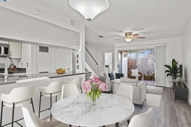 dining room with ceiling fan, sink, a textured ceiling, and light hardwood / wood-style flooring