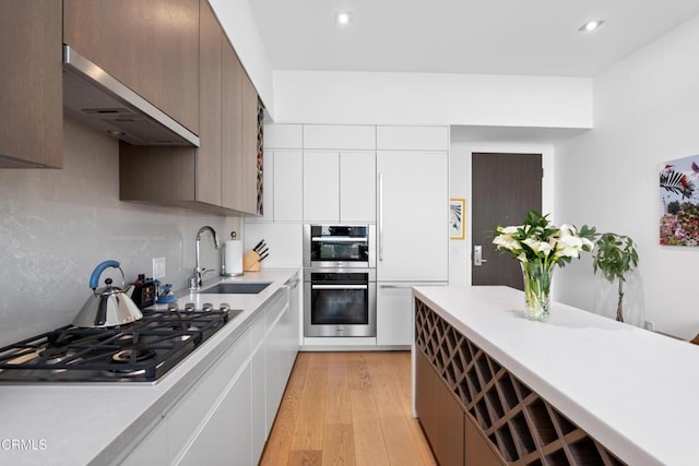 kitchen featuring wall chimney range hood, light hardwood / wood-style floors, sink, white cabinetry, and appliances with stainless steel finishes