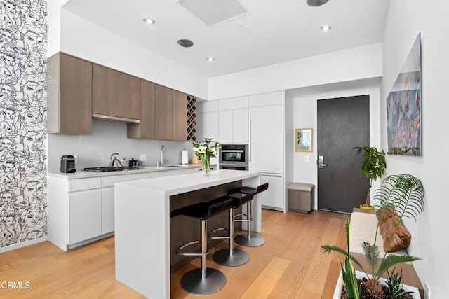 kitchen with stainless steel gas cooktop, light wood-type flooring, white cabinetry, and a center island