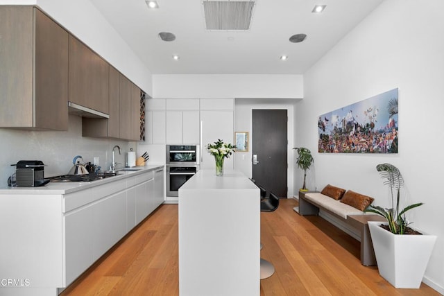 kitchen with white cabinetry, light hardwood / wood-style floors, appliances with stainless steel finishes, a center island, and sink