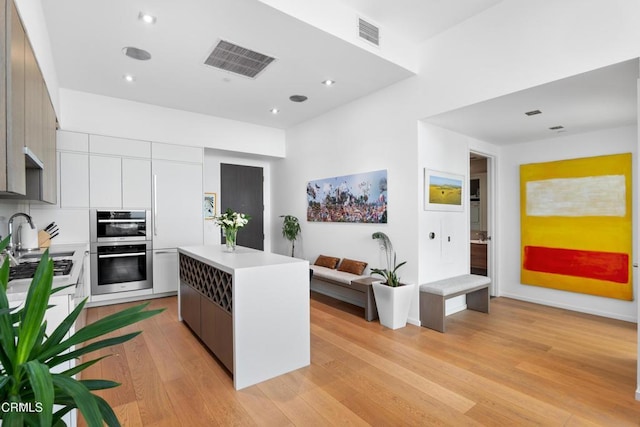 kitchen featuring a kitchen island, sink, light wood-type flooring, gray cabinetry, and stainless steel double oven