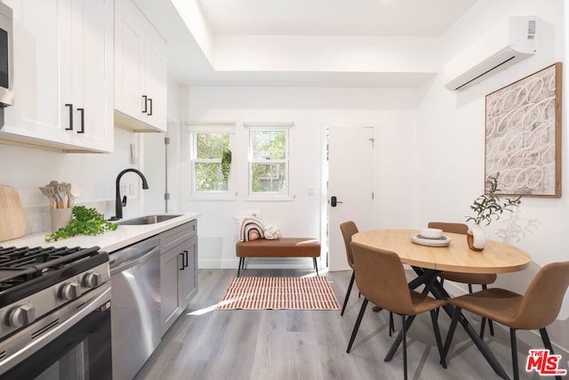 kitchen featuring appliances with stainless steel finishes, an AC wall unit, white cabinetry, sink, and light wood-type flooring