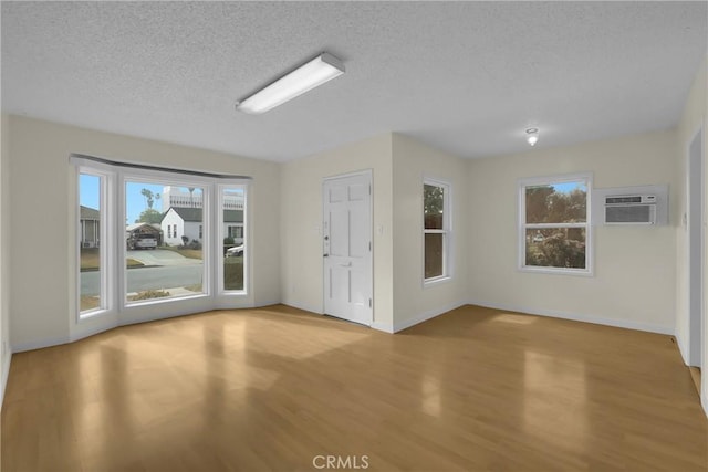 spare room featuring a wall unit AC, a textured ceiling, and light wood-type flooring