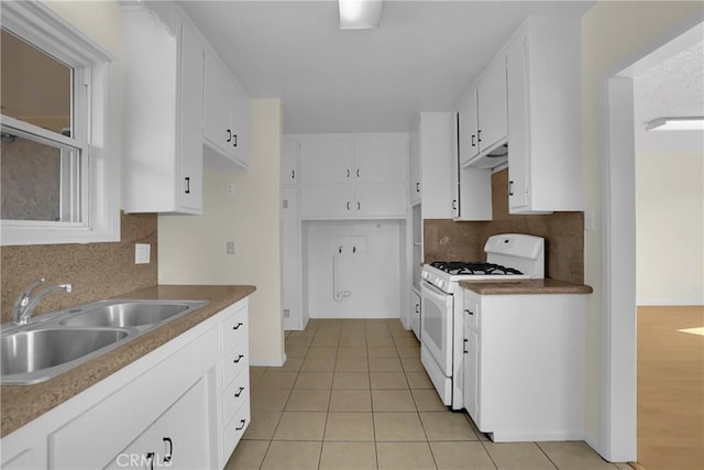 kitchen with light tile patterned floors, white range with gas stovetop, tasteful backsplash, white cabinets, and sink