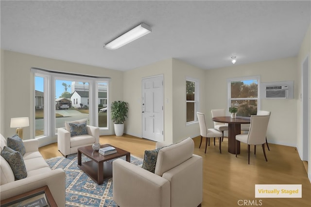 living room featuring a textured ceiling, light wood-type flooring, a wall mounted AC, and a healthy amount of sunlight