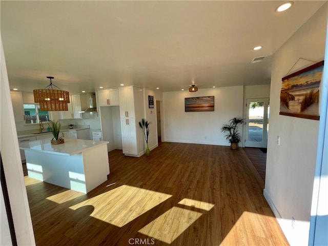 kitchen featuring dark wood-type flooring, white cabinetry, hanging light fixtures, a center island, and wall chimney exhaust hood