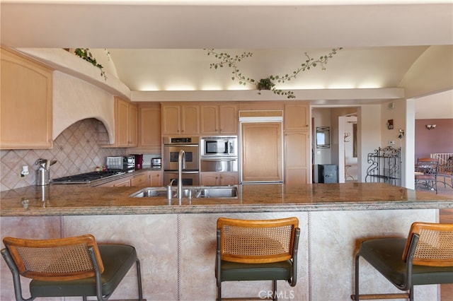 kitchen featuring built in appliances, decorative backsplash, sink, light brown cabinetry, and kitchen peninsula